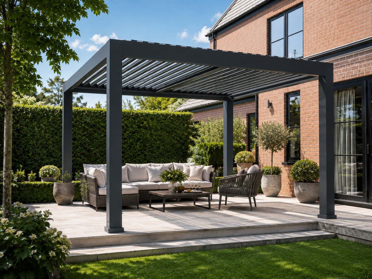 A modern anthracite colour outdoor pergola over a paved patio with a sectional sofa, armchair, and coffee table, set in a landscaped backyard with a brick house, green hedges, and lawn.